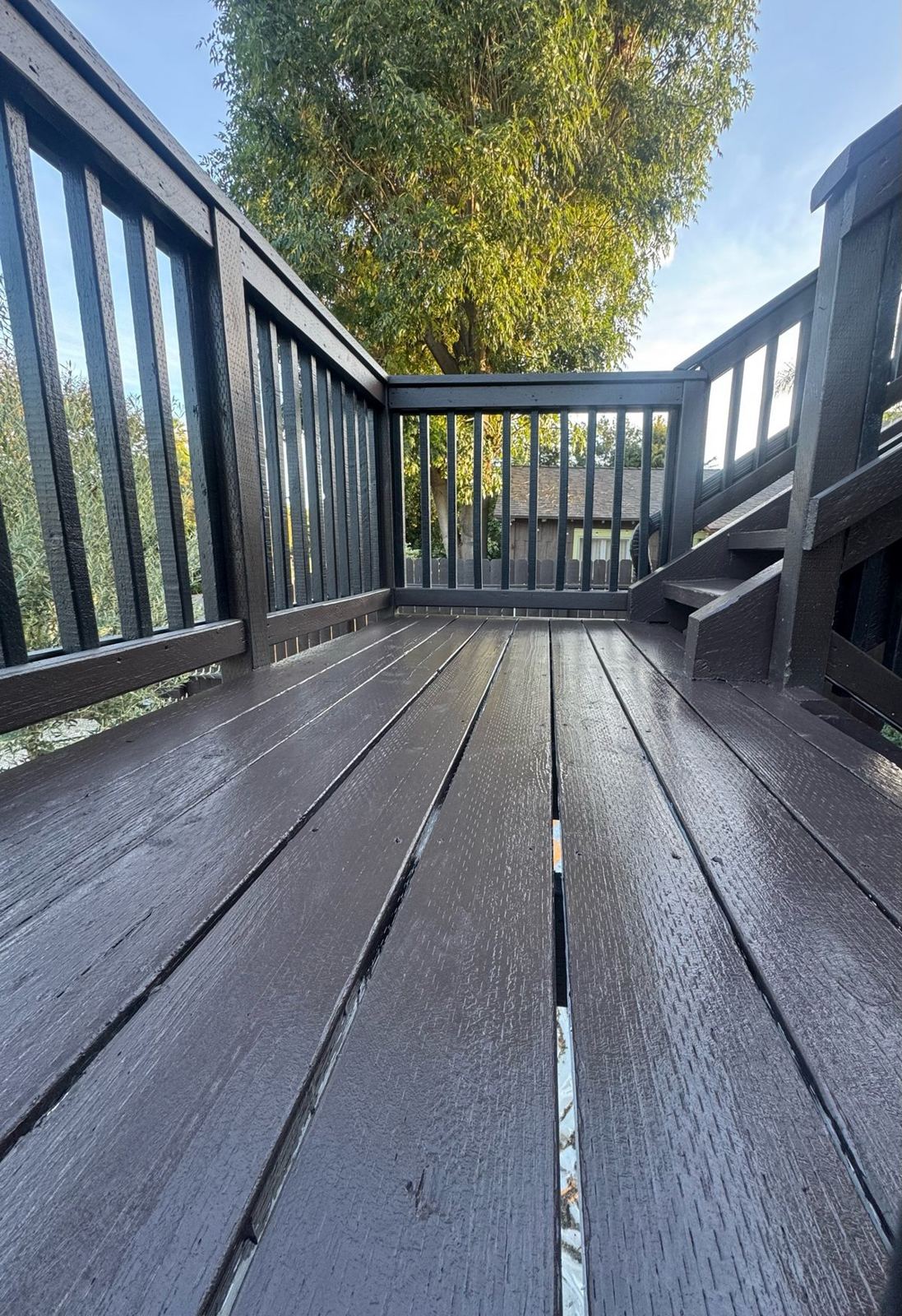Finished deck with fresh dark coating on boards and railings after repair