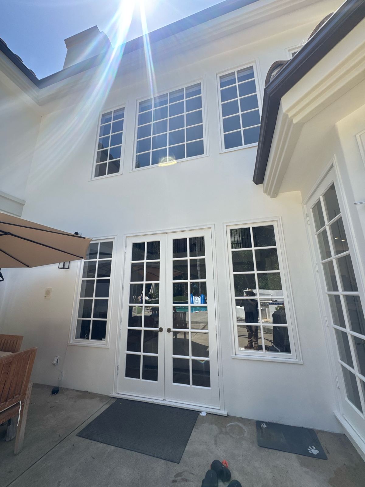 White two-story rear exterior of a home with French doors and tall grid windows in bright sun