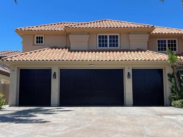 Finished stucco home exterior with tile roof and three black garage doors under a blue sky