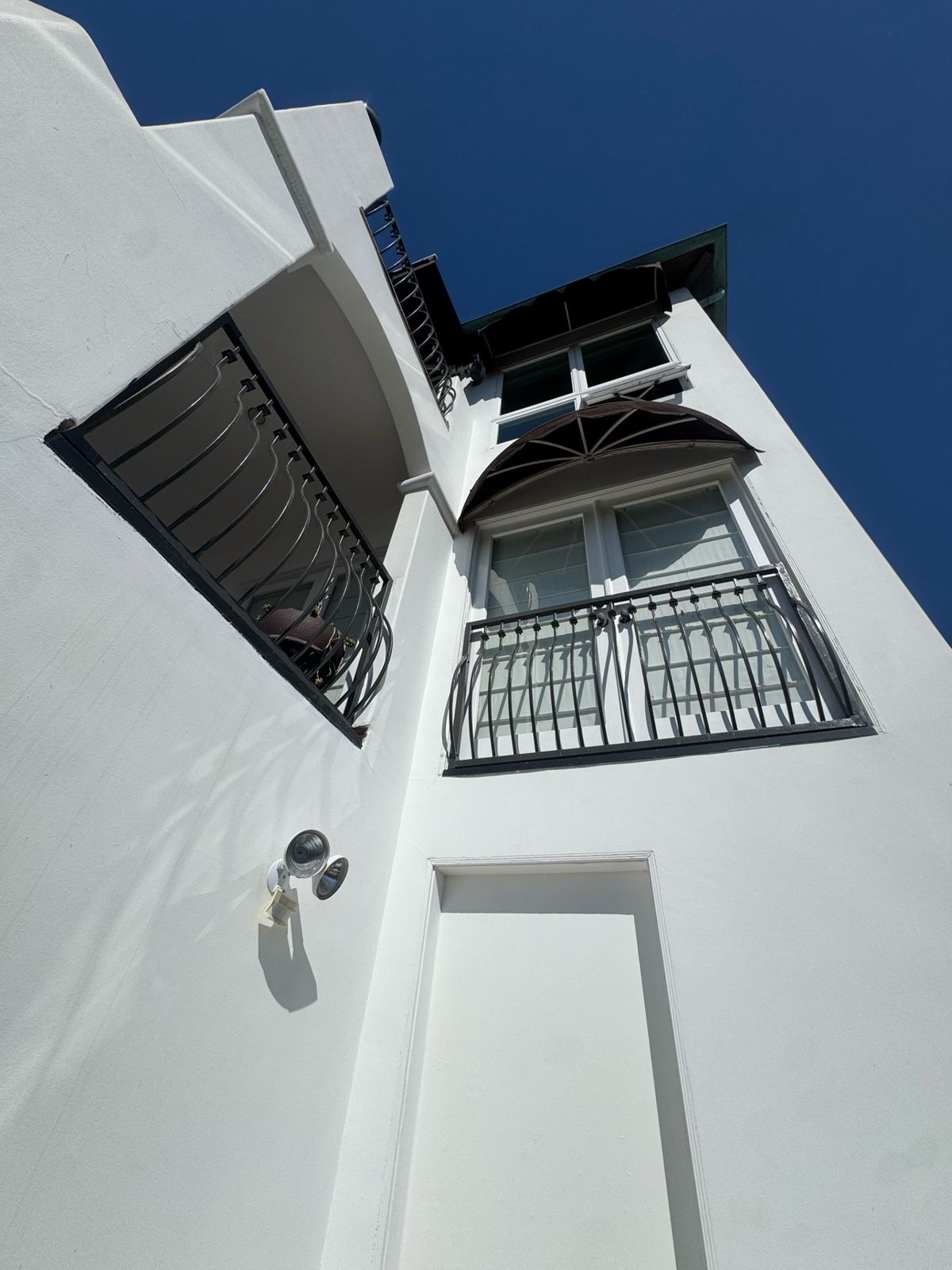 Tall white painted home exterior with black balcony railings under a clear blue sky