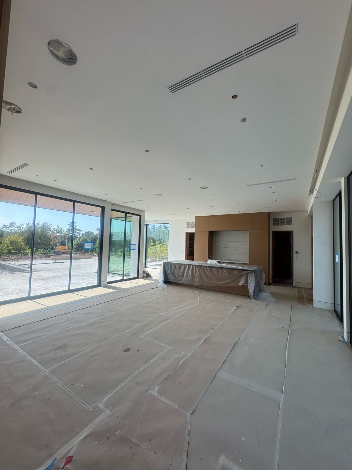 Open great room and kitchen with freshly painted white ceiling and walls, kitchen island covered, and floors protected during painting