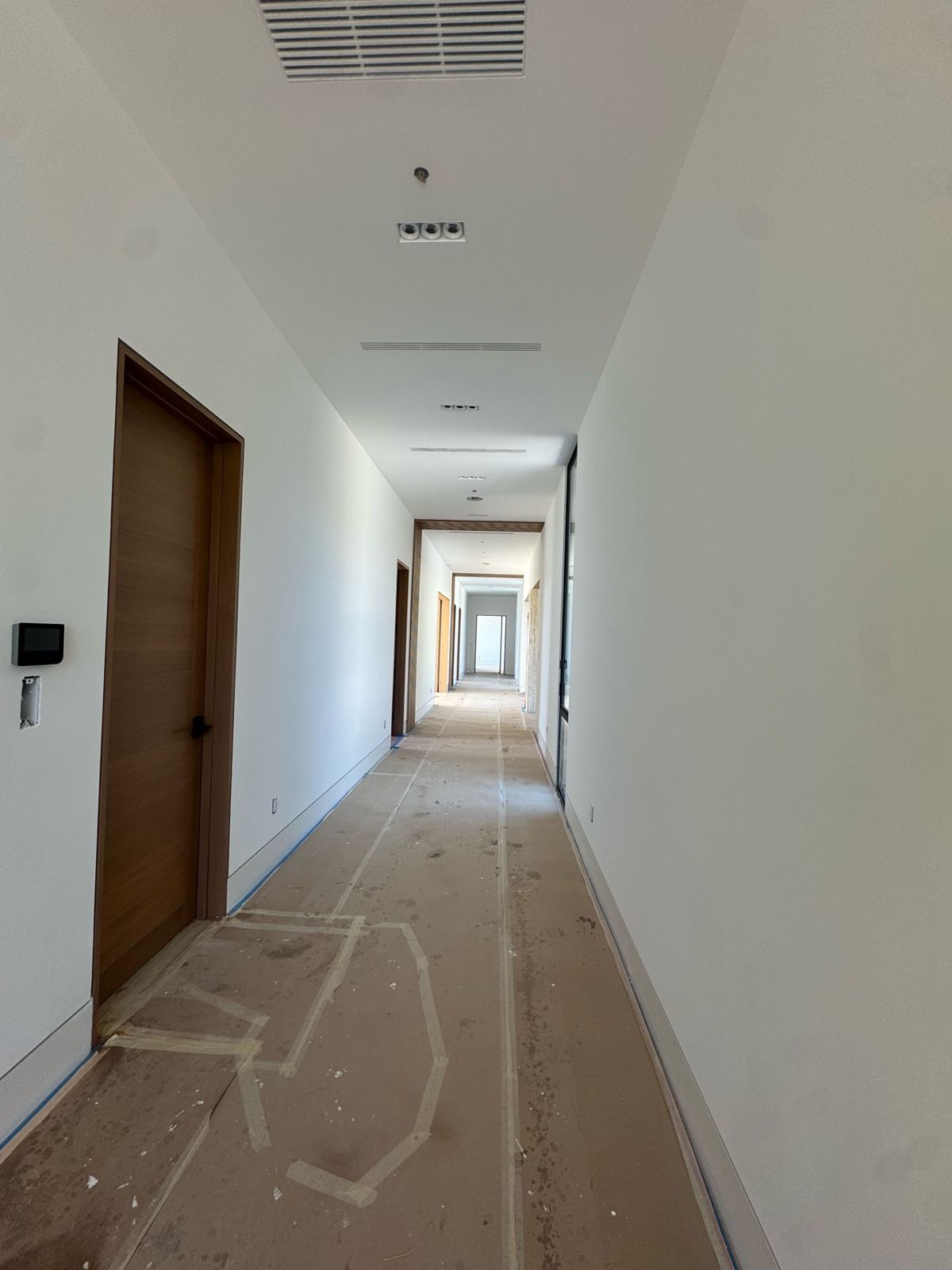 Long hallway with smooth freshly painted white walls and ceilings, wood doors, and floors protected with paper during painting