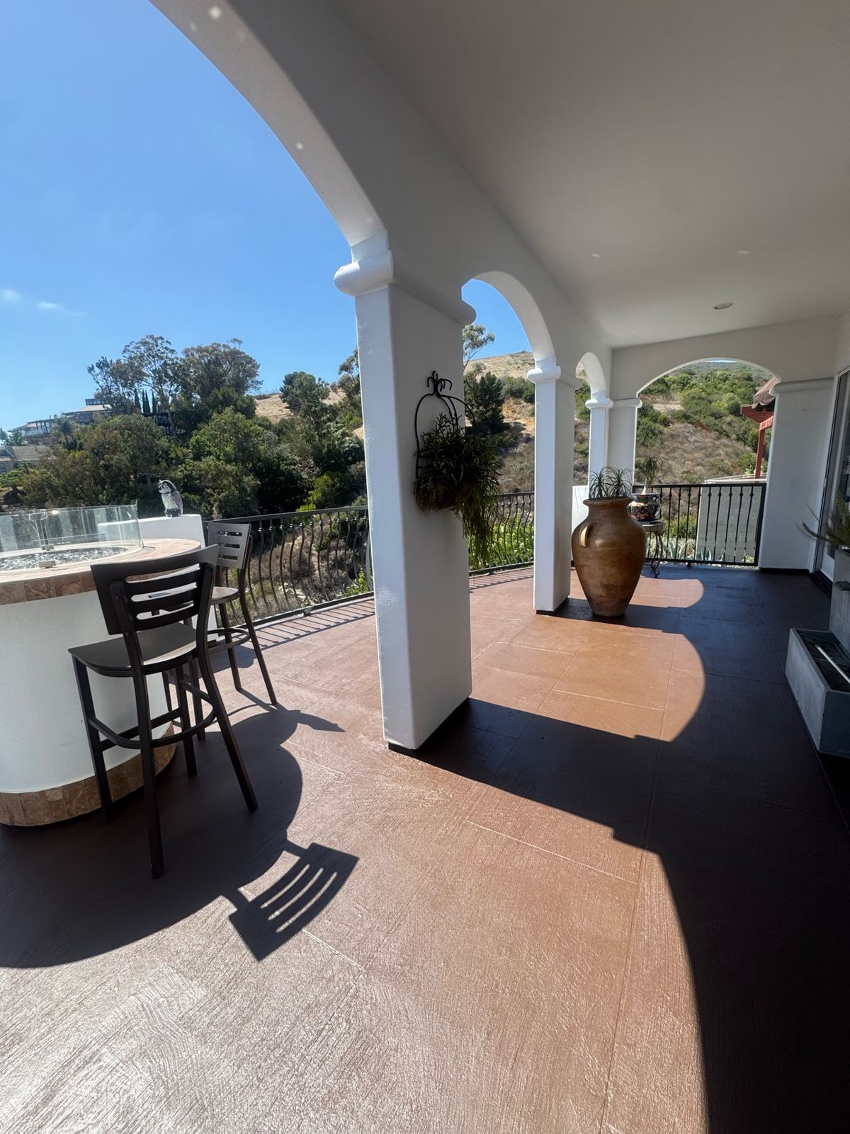 Covered balcony terrace with white painted stucco arches and columns and a coated brown floor overlooking hills