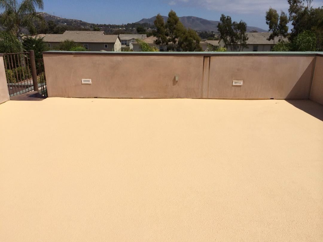 Rooftop deck with a fresh beige coated surface and stucco parapet walls under a blue sky