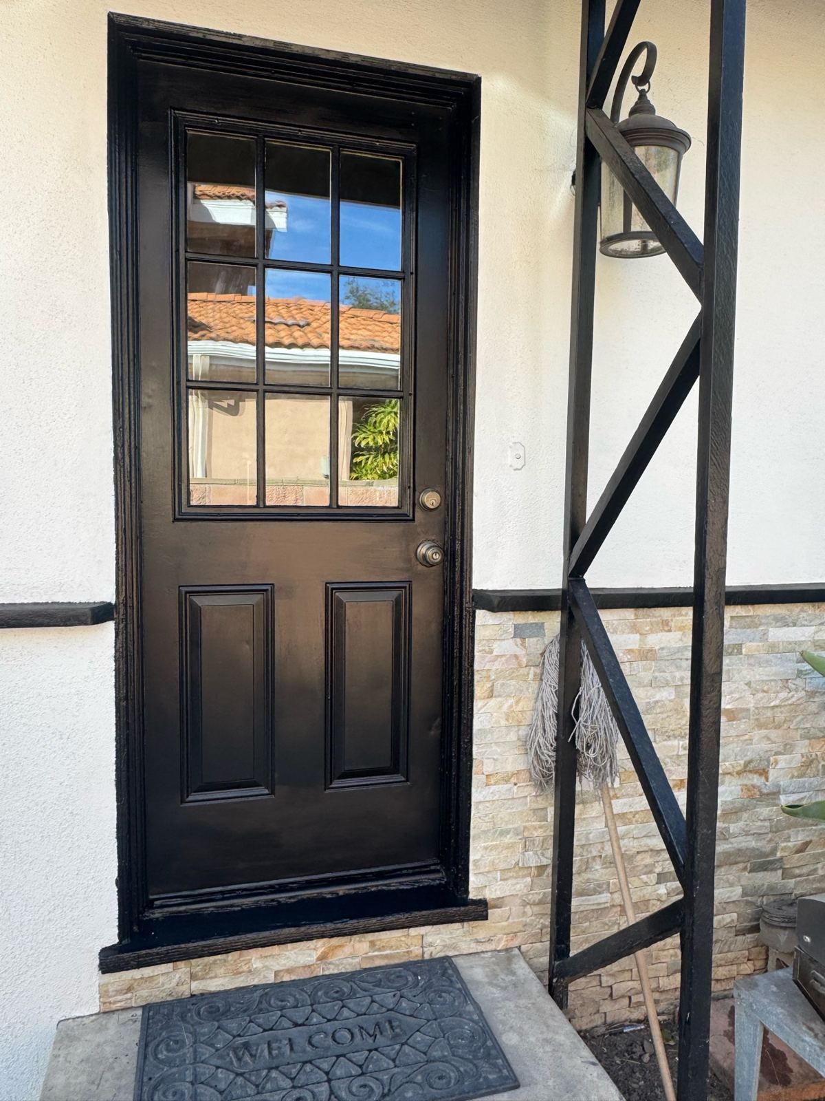 Front door freshly painted black with glass panes, stone veneer, and matching black trim