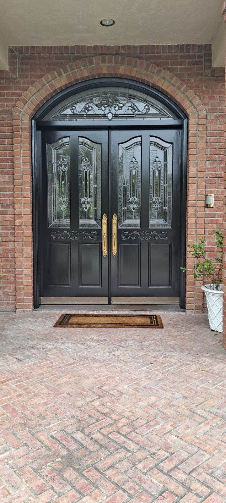 Black double entry doors with decorative glass panels and brass handles set in a red brick arched entry