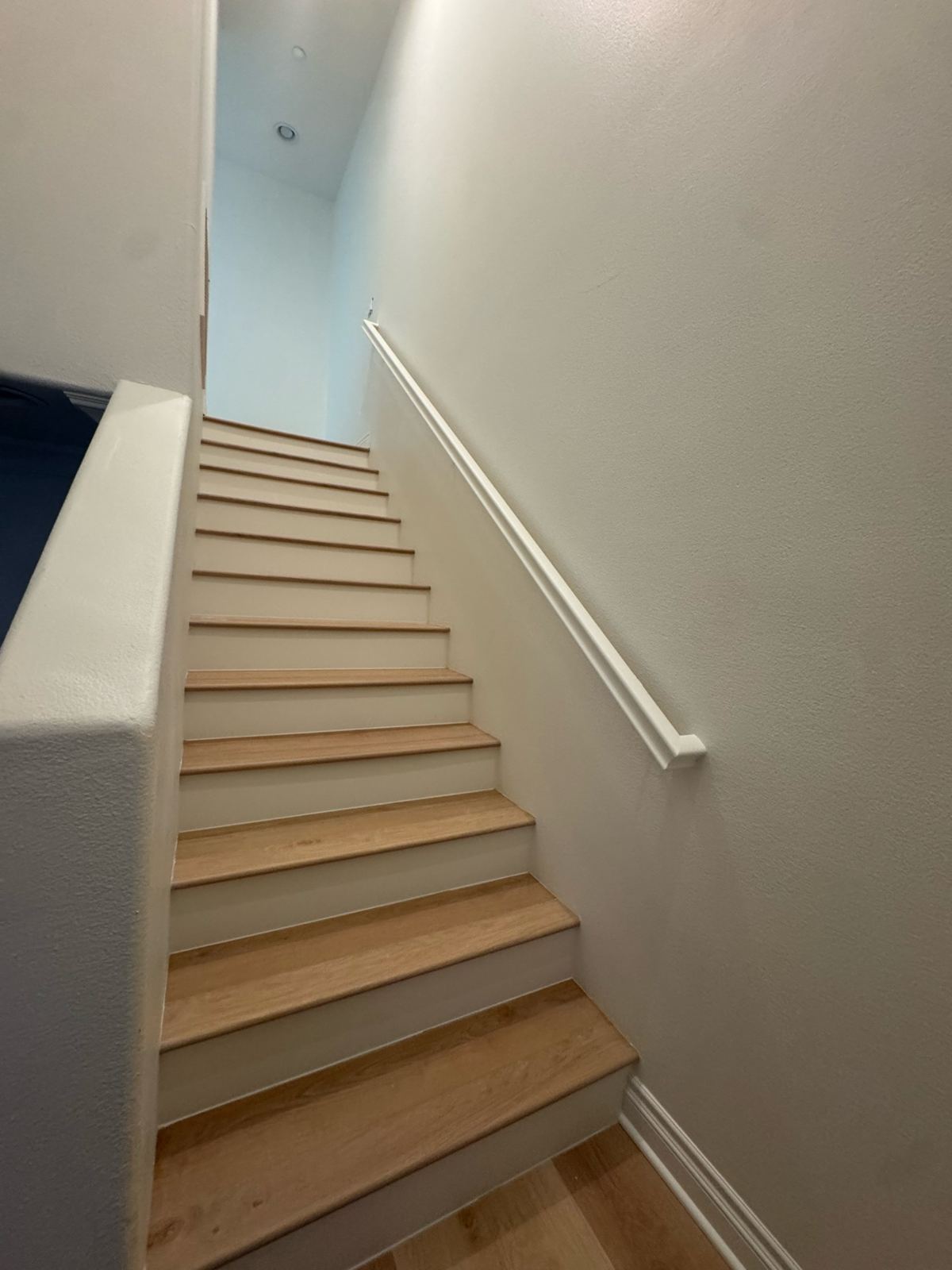 Interior staircase with natural wood treads, white painted risers, walls, and handrail