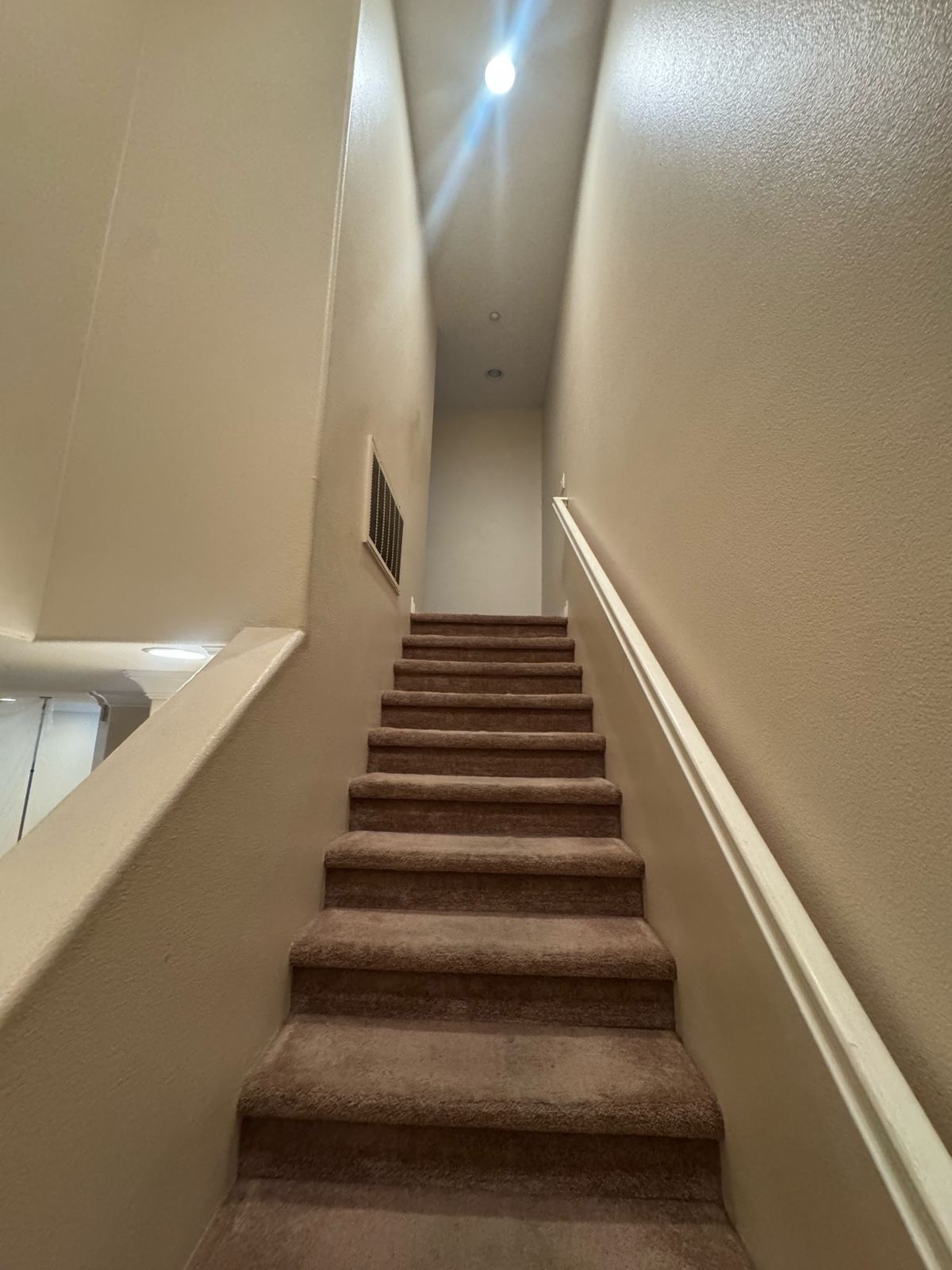 Tall interior stairwell with freshly painted warm cream walls, white handrail, and carpeted steps