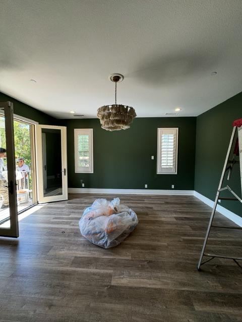 Room with deep green painted walls, white trim, and wood plank flooring under a beaded chandelier