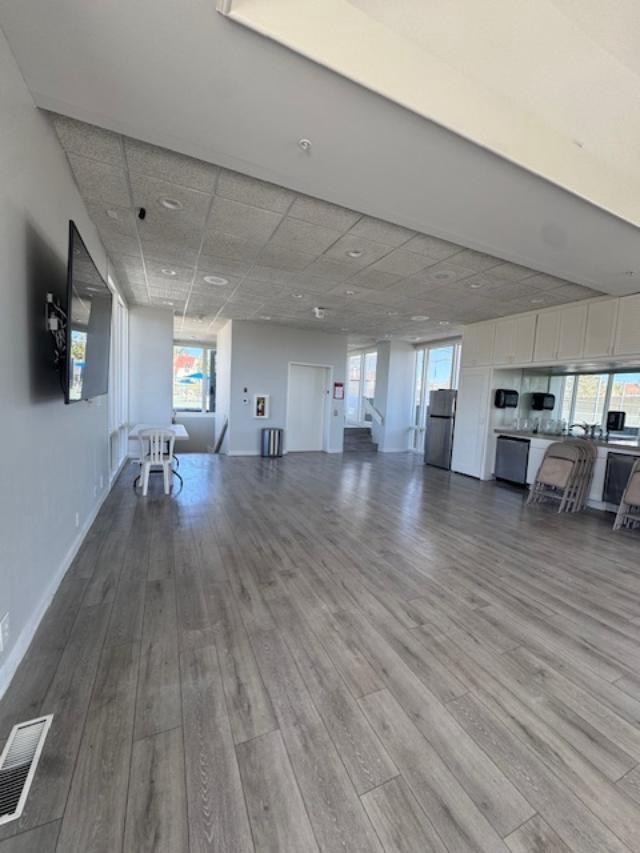 Large community room with gray plank flooring, light painted walls, and white kitchen cabinets