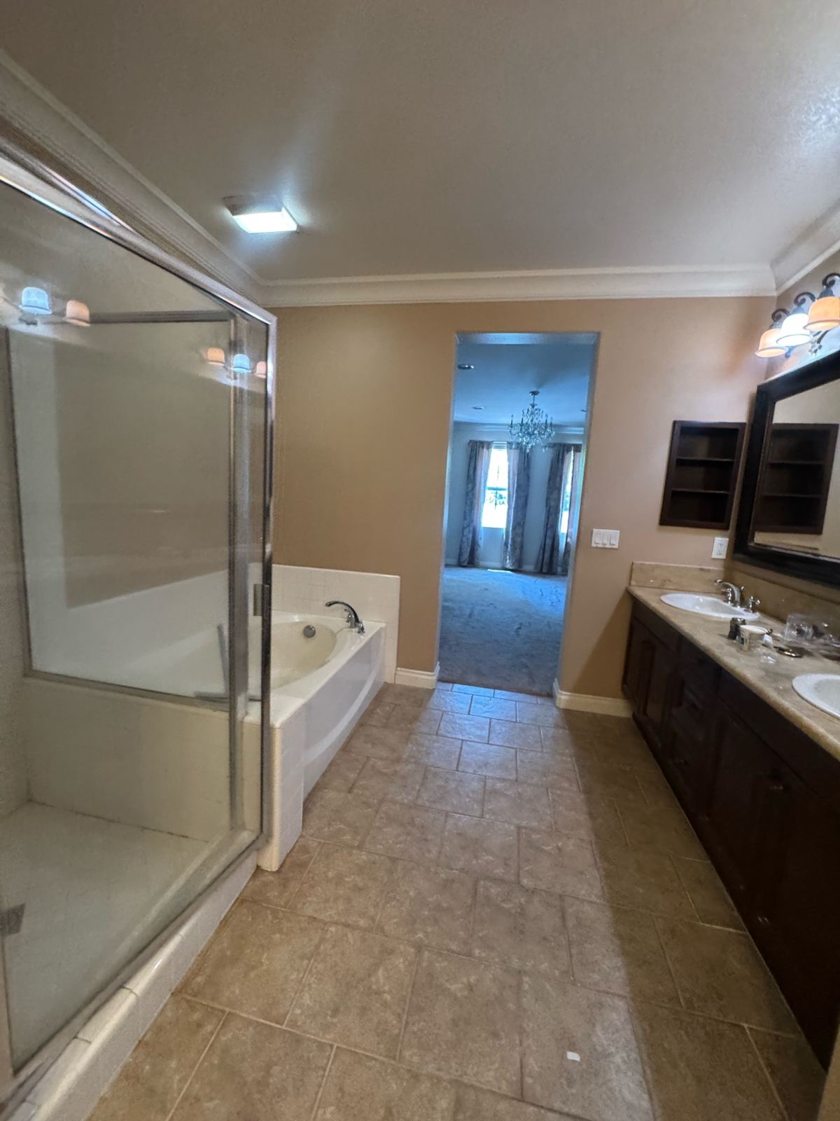 Primary bathroom with warm tan painted walls and ceiling, dark wood double vanity cabinets, tub, and glass shower
