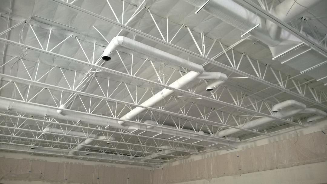 Commercial ceiling with steel trusses, ducts, and pipes all painted white in an open-ceiling space