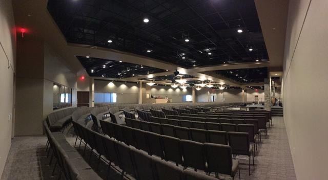 Auditorium interior with a black painted ceiling, warm walls, stage lighting, and rows of seating