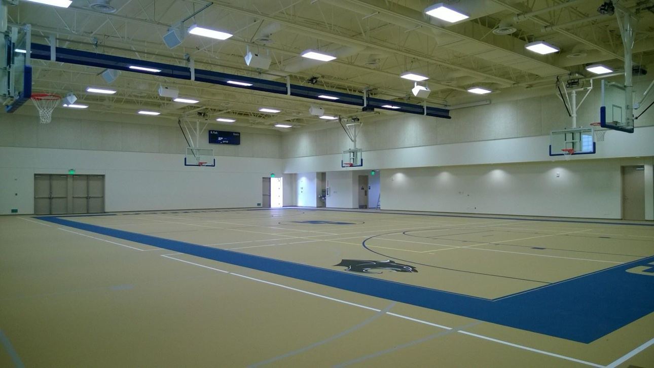 School gymnasium and basketball court from a second angle, with painted walls, ceiling trusses, and hoops