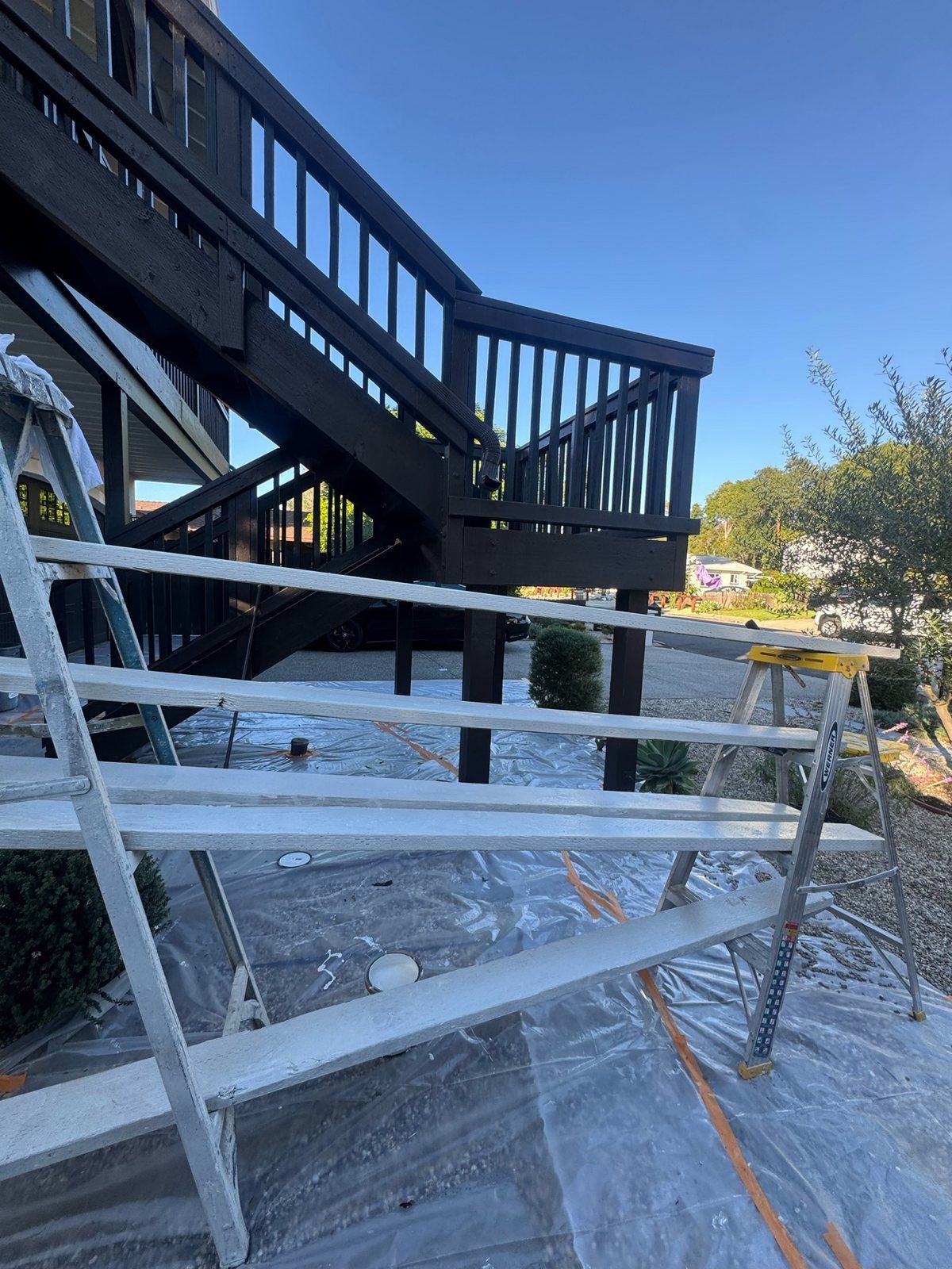 Two-story deck and staircase project mid-finish, with new primed boards staged on ladders