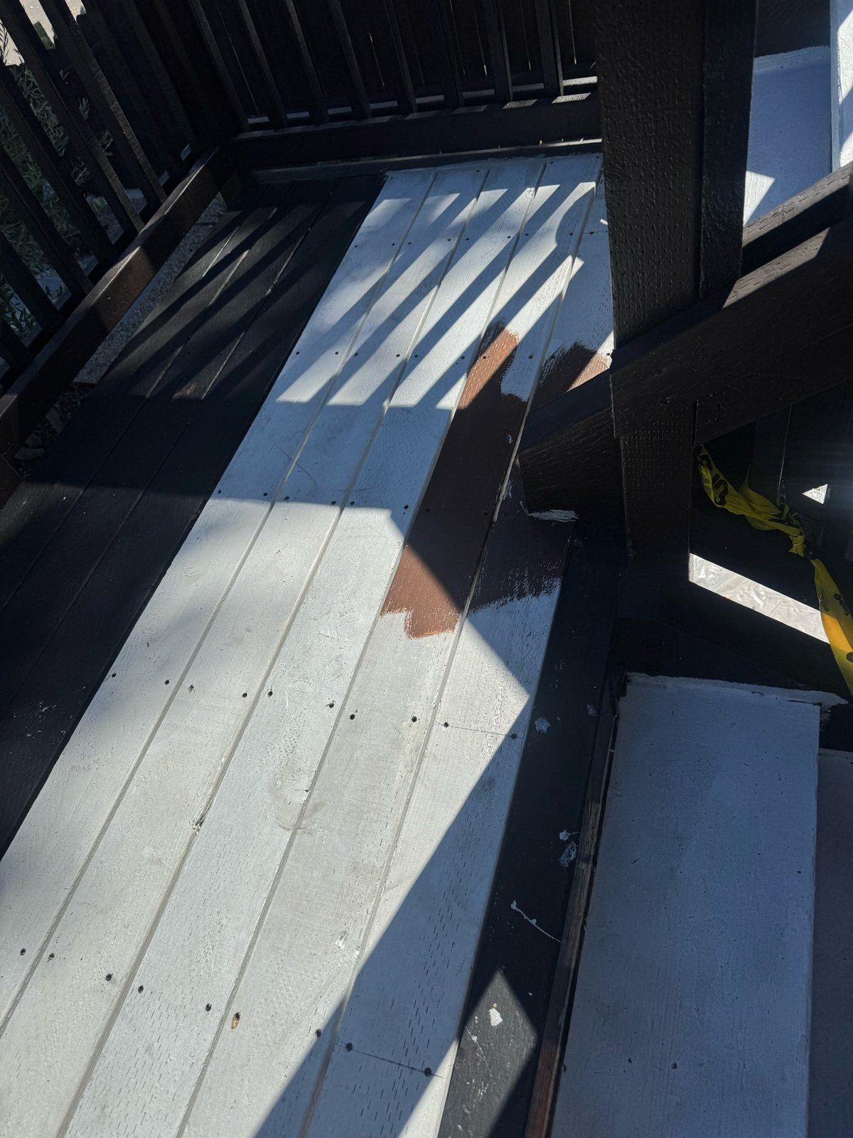 Deck boards mid-coat, with the new dark finish going over primed replacement boards