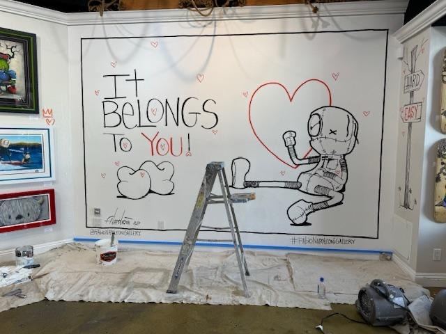 Gallery wall mural being painted, with a ladder, drop cloths, and paint supplies on the floor
