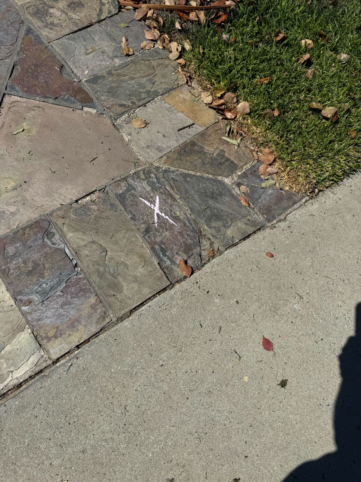 Before photo of a cracked slate tile marked with a chalk X along the sidewalk edge