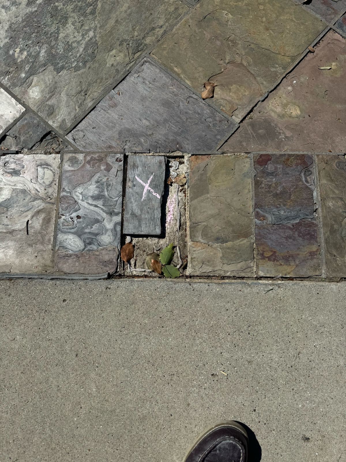 In-progress photo of a marked slate tile lifted out of the driveway, exposing the mortar bed