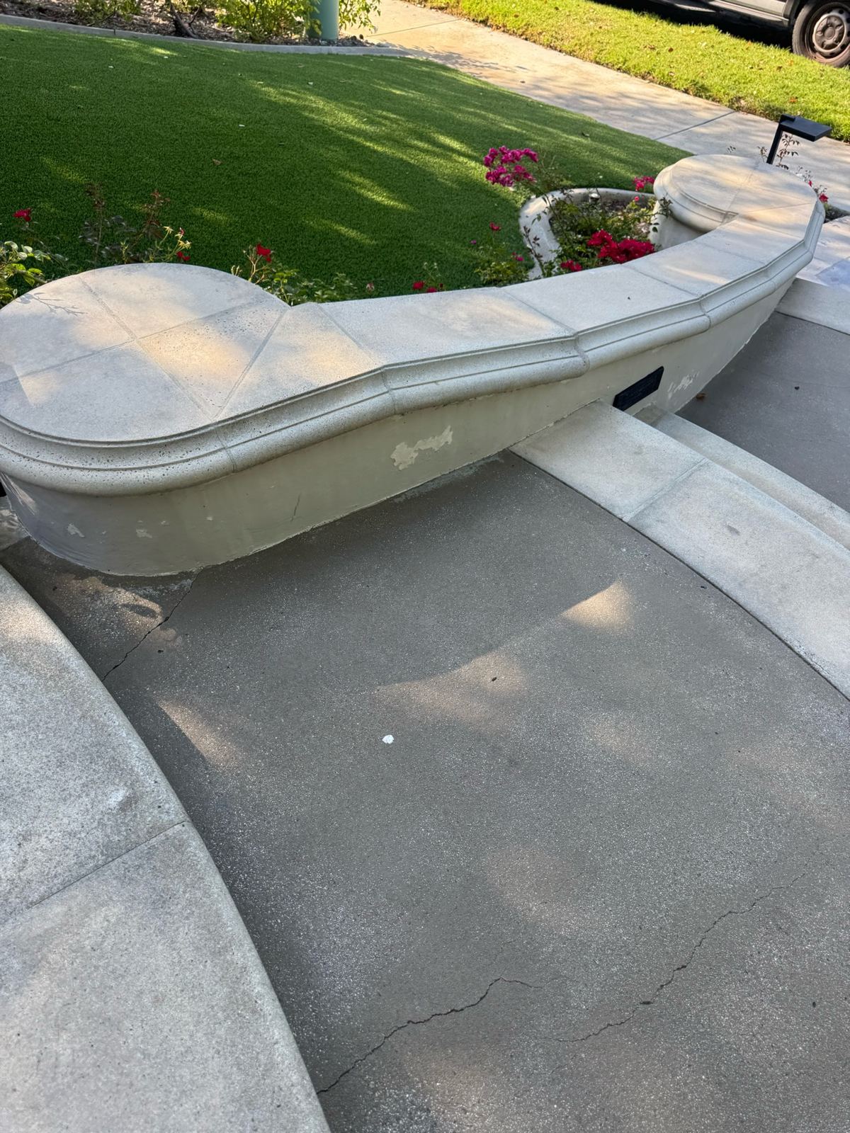 Before photo of a curved concrete planter wall with peeling stucco and a cracked concrete walkway beside the lawn